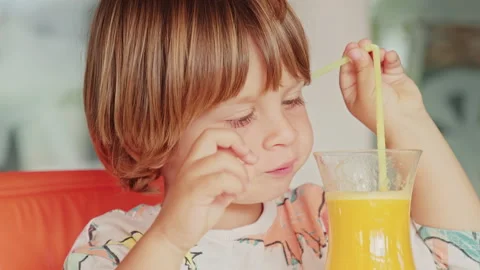 Laughing kid drinks freshly squeezed orange juice through a straw in the kitchen Stock Footage 163244270