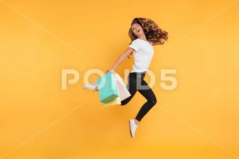 Laughing pretty young woman jumping holding shopping bags. Stock Photos
