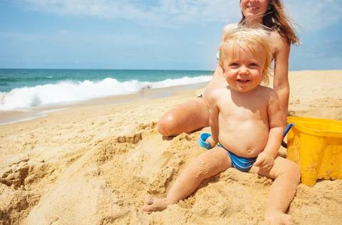 Laughing toddler boy sit on the beach and smile Stock Photos