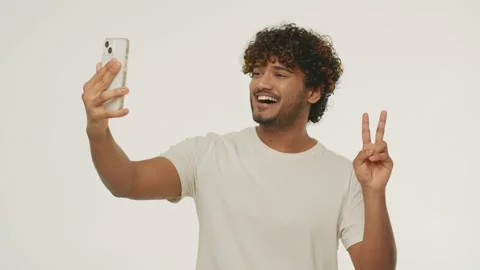 Laughing young man with smartphone gesturing during video call. Smiling mixed Stock Footage 231674114