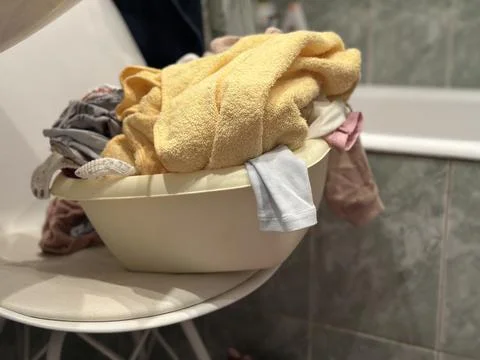 Laundry Basin Full of Clothes and Towels on a Chair Stock Photos