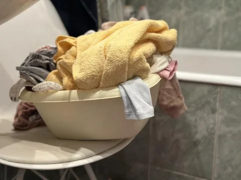 Laundry Basin Full of Clothes and Towels on a Chair Stock Photos