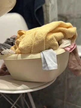 Laundry Basin Full of Clothes and Towels on a Chair Stock Photos