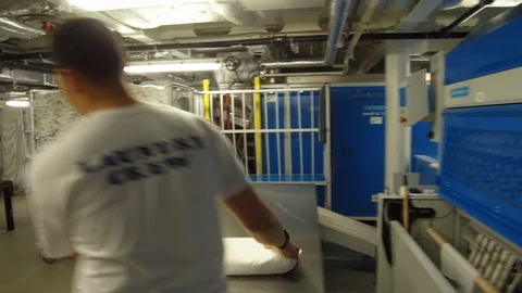 Laundry crew member arranging clean folded sheets on rack at cruise ship Stock Footage 117750673