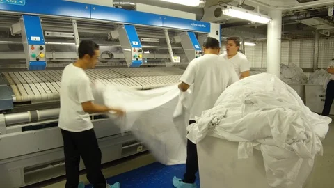 Laundry crew members inserting sheets in cruise ship laundry machine Stock Footage 117750821