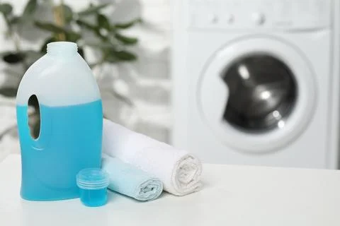 Laundry detergent, cap and rolled towels on white table in bathroom, space .. Stock Photos