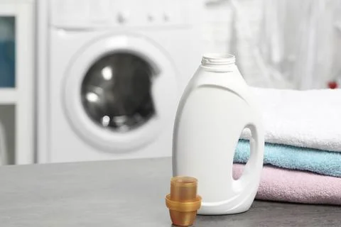 Laundry detergent, cap and stacked clean towels on grey table, space for text Stock Photos