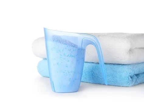 Laundry detergent in plastic measuring cup and towels on white background Stock Photos