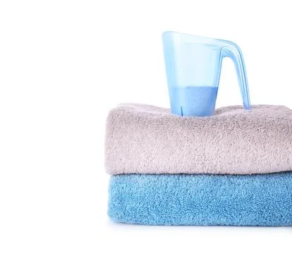 Laundry detergent in plastic measuring cup and towels on white background Stock Photos