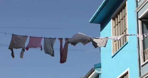Laundry hanging on a clothesline beside a bright blue building, clear sky. Stock-Footage 320028131