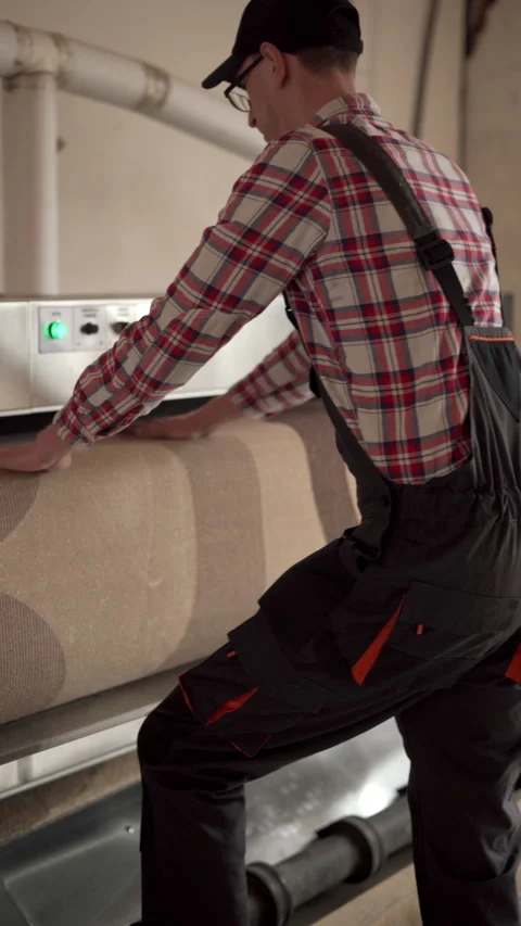 Laundry worker in cap and overalls working on automatic machine for carpet Stock Footage 269761481