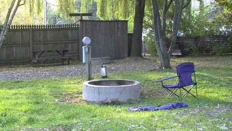 Lawn chair faces a fire pit in a green rural yard Video stock 91056002
