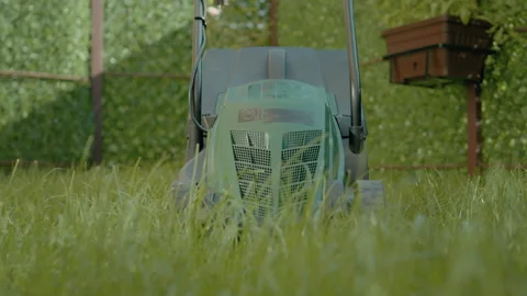 Lawn mower ready for grass cutting on terrace overgrown with tall grass Stock Footage 318832074