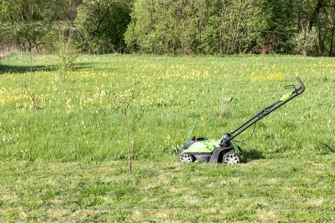 Lawn mower on the site that needs to be mowed from the grown grass Stock Photos