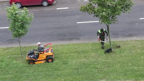 Lawn mowing. One worker operates a self-propelled mower, the other a manual p Stock Footage 138140258