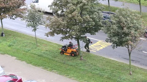 Lawn mowing. One worker operates a self-propelled mower, the other a manual p Stock Footage 138140453