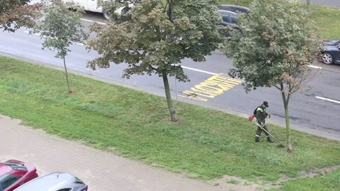 Lawn mowing. Worker with a trimmer in his hands. Mows the grass on the side o Stock Footage 138140616