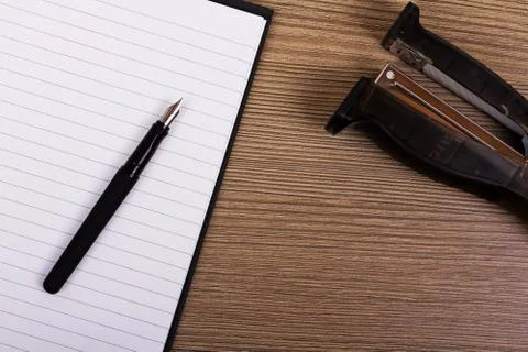 Lay flat image of a notebook and stapler on a wooden surface Stock Photos