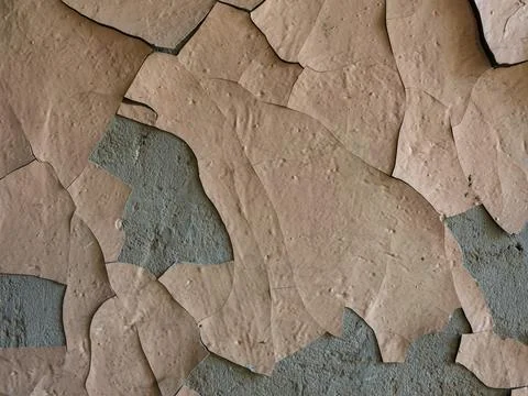 A layer of old beige paint is flaking off the concrete plaster on the wall. Stock Photos