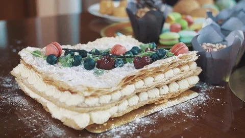 Layered cake decorated with berries, mint and candy on table with bakery Video stock 77160553