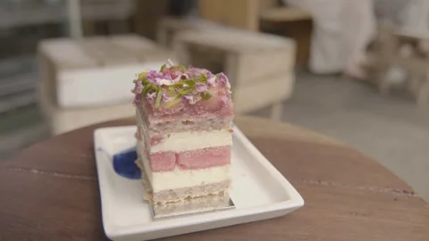 Layered Cake Slice with Floral Garnish Served at Outdoor Cafe Table in Sydney Stock Footage 345654911