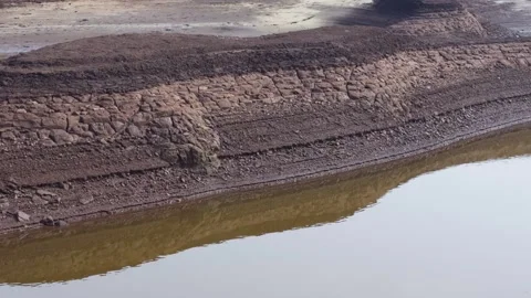 A layered cliff exposing various geological layers next to a body of water Stock Footage 304502606