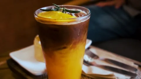 Layered drink of espresso coffee and iced orange juice in a glass with orange Stock Footage 315855243