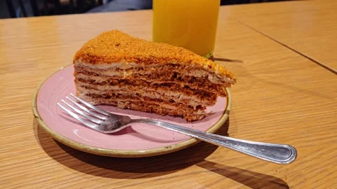 Layered Honey Cake Slice On Pink Plate With Fork And Refreshing Drink On Table Stock Footage 345370428