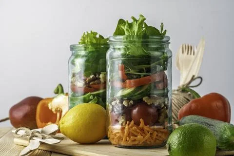 Layered vegetable salad with nuts packed in glass jars on wooden table, Stock Photos