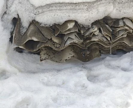 Layers of weathered roofing material partially buried in snow, showcasing t.. Stock Photos