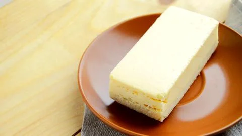 Laying out a brown plate with a rectangular slice of delicious cheesecake clo Stock Photos