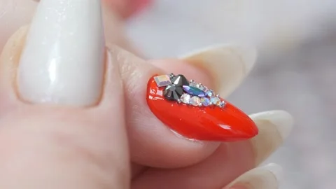 Laying out a pattern of rhinestones on the nail with a spatula and a thin brush. Stock Footage 171290049