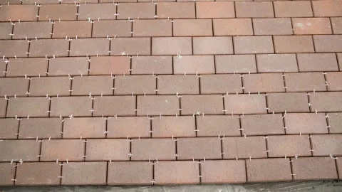 Laying reddish brown clinker tiles in a running bond pattern with white plastic Stock Footage 346656039