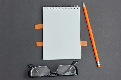 Layout. Gray background. Notepad, pencil, sticks in a notebook, black glasses Stock Photos