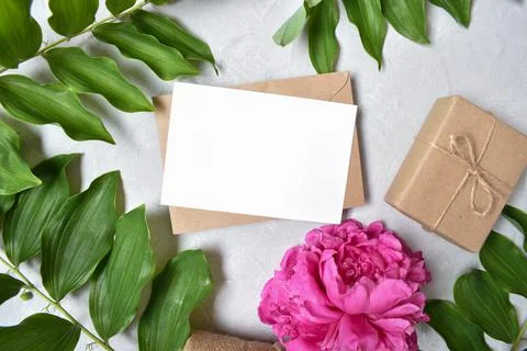 The layout is made of a kraft envelope, a gift and a peony flower on a gray b Foto stock