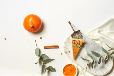 Layout with a piece of pumpkin pie, small pumpkin and green leaves on a white Stock Photos