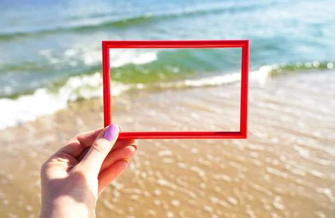 Layout. Red frame in a female hand. Summer sea background. Stock Photos