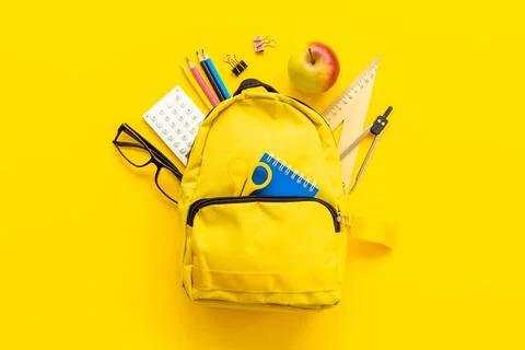 Layout of yellow school backpack full of stationery with apple Stock Photos