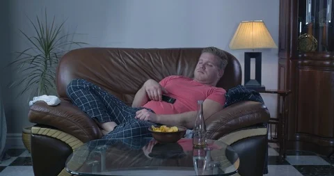 Lazy Caucasian man lying on sofa in front of TV and sleeping. Adult redhead guy Stock Footage