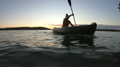 LD Low angle shot of a young woman paddling a kayak at sea in setting sun Stock Footage 136050964