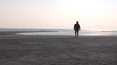 LD Man walking on a sandy beach towards the shoreline at sunset Stock Footage 233991272