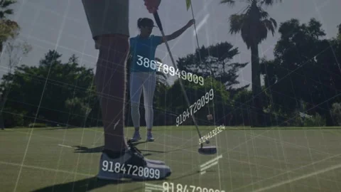 Lead golfer aligning putt, executing stroke to hole while partner lifting flag, Stock Footage 333287649