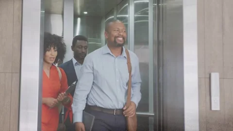Lead man stepping through elevator doors opening, team following, tablet showing 库存影片 333859621