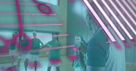 Leading coach in polo holding timer, briefing green-vested team in gym under Stock Photos