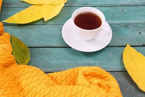 Leaf fall mood, white cup of coffee with a knitted scarf and fallen leaves on Stock Photos