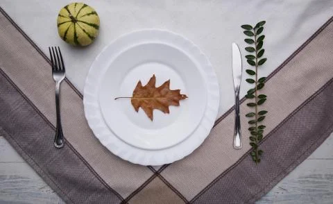 Leaf on a plate, fork and knife on a tablecloth next to a pumpkin Stock Photos