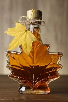 Leaf shaped bottle of tasty maple syrup on wooden table Stock Photos