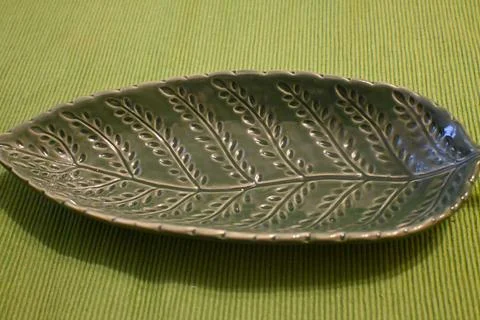 Leaf-shaped ceramic plate on green textile Stock Photos
