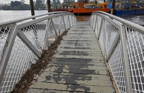 A leaf strewed floating bridge with industry background on the Brisbane River Stock Photos