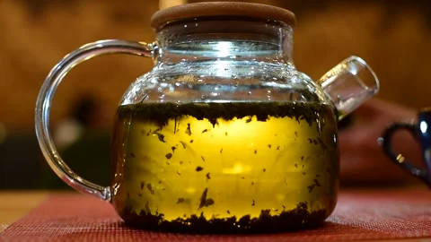 Leaf tea floats in boiling water in a clear glass teapot. Stock Footage 156498475